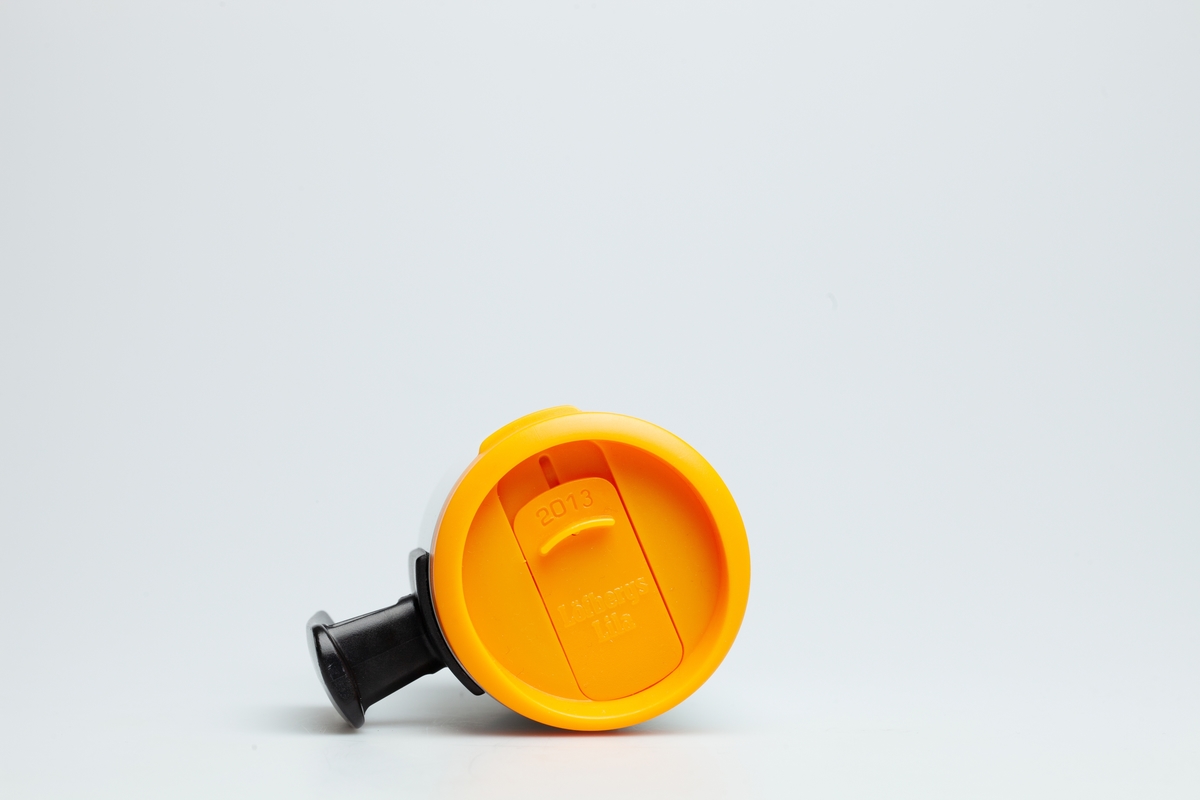 Et oransje skrulokk til en Statoilkopp fra 2013. En mekanisme i lokket kan åpne og lukke for et lite hull, der kan man drikke kaffe gjennom. På skrulokket står det 2013 og Löfbergs Lila.