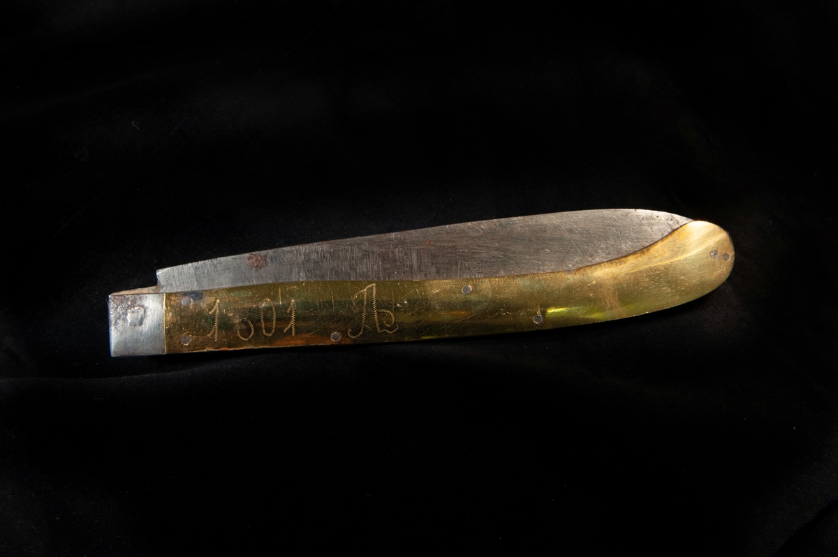 Större kniv i fällknivsmodell i järn och mässingshandtag, del i ett set med JM.09855. Benämns som "gästabudstyg" i orginalkatalog.
Graverat "1801 A" på ena sidan, och "SMD" på andra. Stämplar saknas.