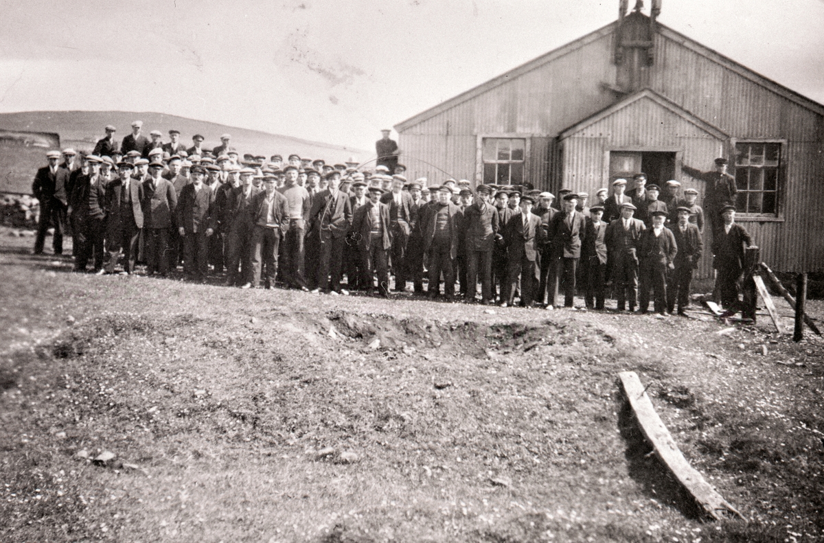 Enligt tidigare noteringar: "Bohuslänska fiskare utanför Svenska Kyrkan i Baltasound, Shetland, pingstdagen 1933. 
Repro av foto tillhörande Ernst Gullman".