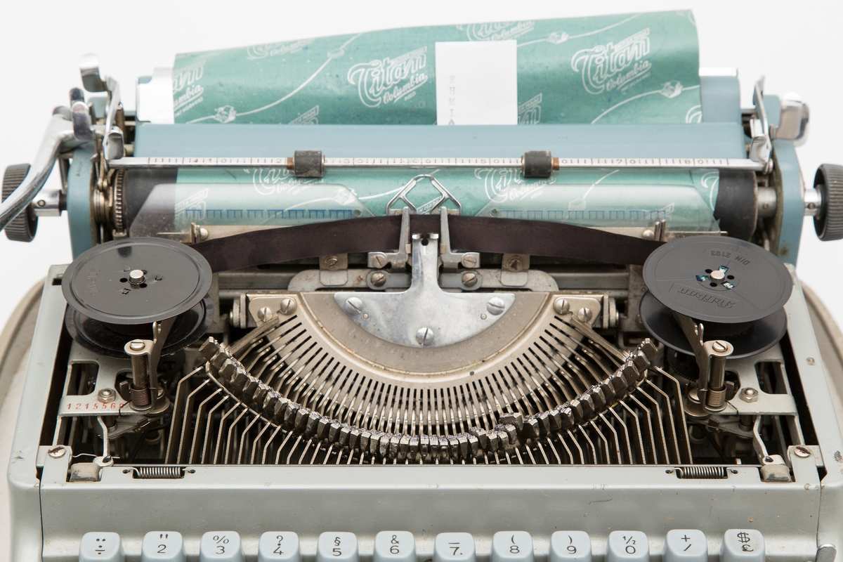 Transportabel skrivemaskin i metall og plast. Skrivemaskinen er fastmontert i koffertbunnen, men kan løftes av. Har avtagbart lokk med bærehåndtak. Transportabel, men relativt stor og tung. En nøkkel følger med.