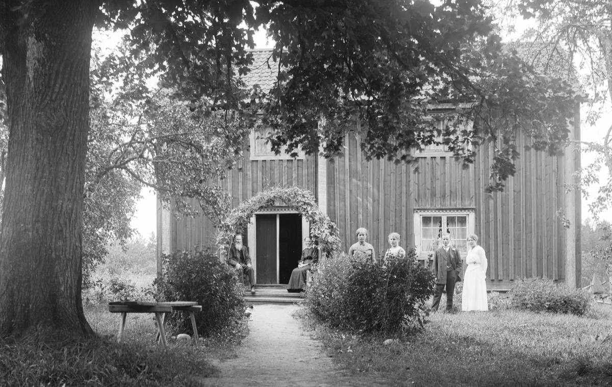 Torpet Erstorp under Fundshult i Svinhult socken. På den lövade farstubron sitter torparen Johan Edvard Carlsson och hustrun Klara Svensson. Möjligtvis firar de bröllopsdag med barnen och släkt. Foto från något år under 1920-talet.