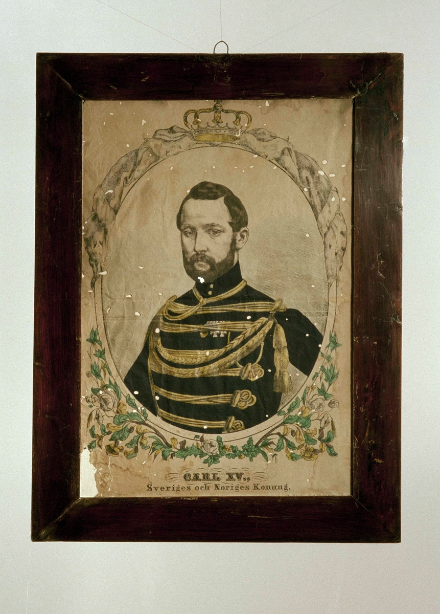 Färglitografi i glas och ram, föreställande " Carl XV Sveriges och Noriges Konung ". Porträtt i halvfigur, oval inramning med bladornament, krönt av krona. Mahognybetsad slät träram.