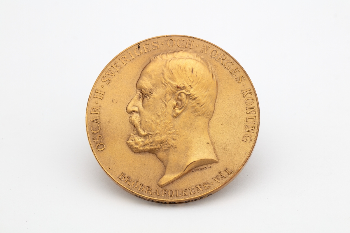 Rund medalje i etui. Kong Oscar IIs portrett i profil og hans valgspråk "BRÖDRAFOLKENS VÄL".