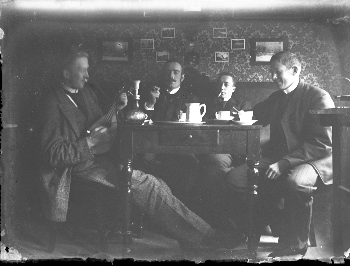 Gruppeportrett av menn rundt bord med mandolin og vannpipe.

Antatt fotosamling etter Anders Johnsen.