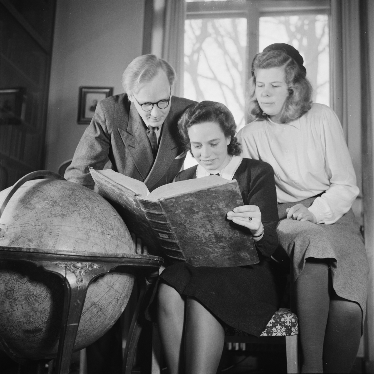 En man och två kvinnor tittar i en bok, Östgöta nation inför restaurering, Uppsala 1946