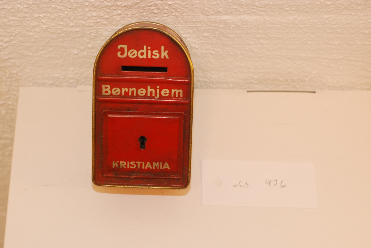 Liten pengekasse / bøsse formet som en postkasse, med teksten: "Jødisk Børnehjem Kristiania". Brukt til innsamling for etableringen av det jødiske barnehjemmet i Kristiania i 1924.