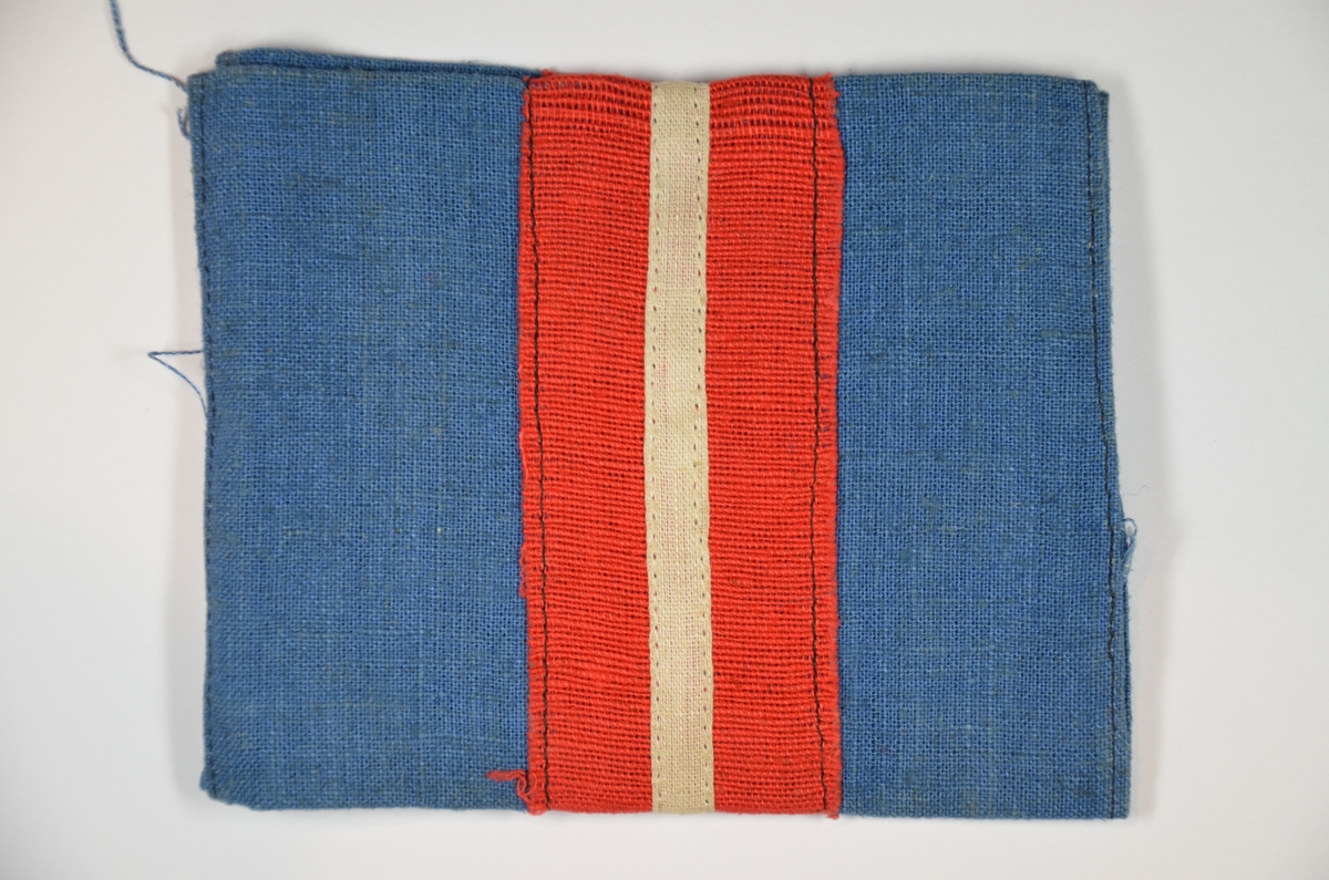Tøy-armbind i blått med rød og hvit midt-stripe. Brukt av den danske hjemmefronten under krigens sluttdager.