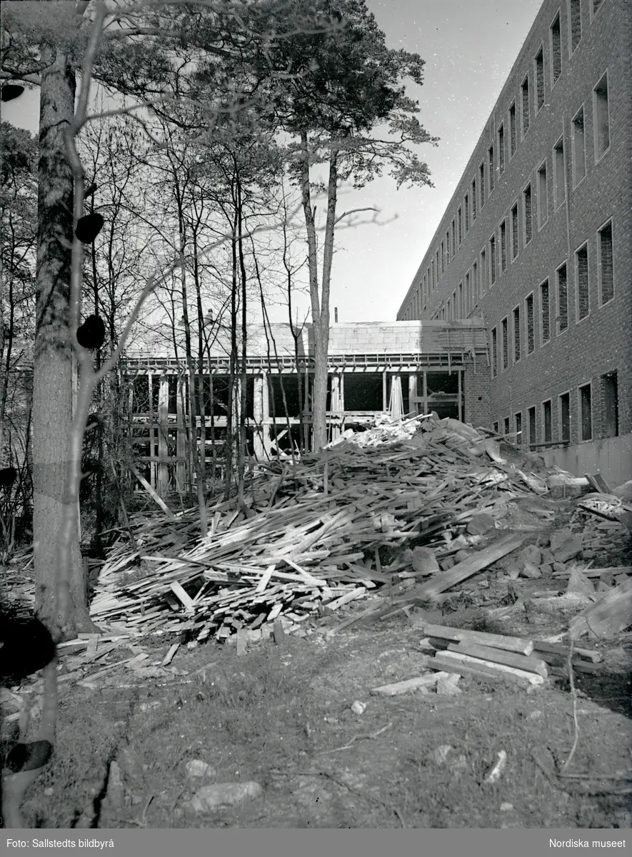 Byggande av Solna läroverk 1946. Fasader av läroverket med byggmaterial liggande mellan träd.