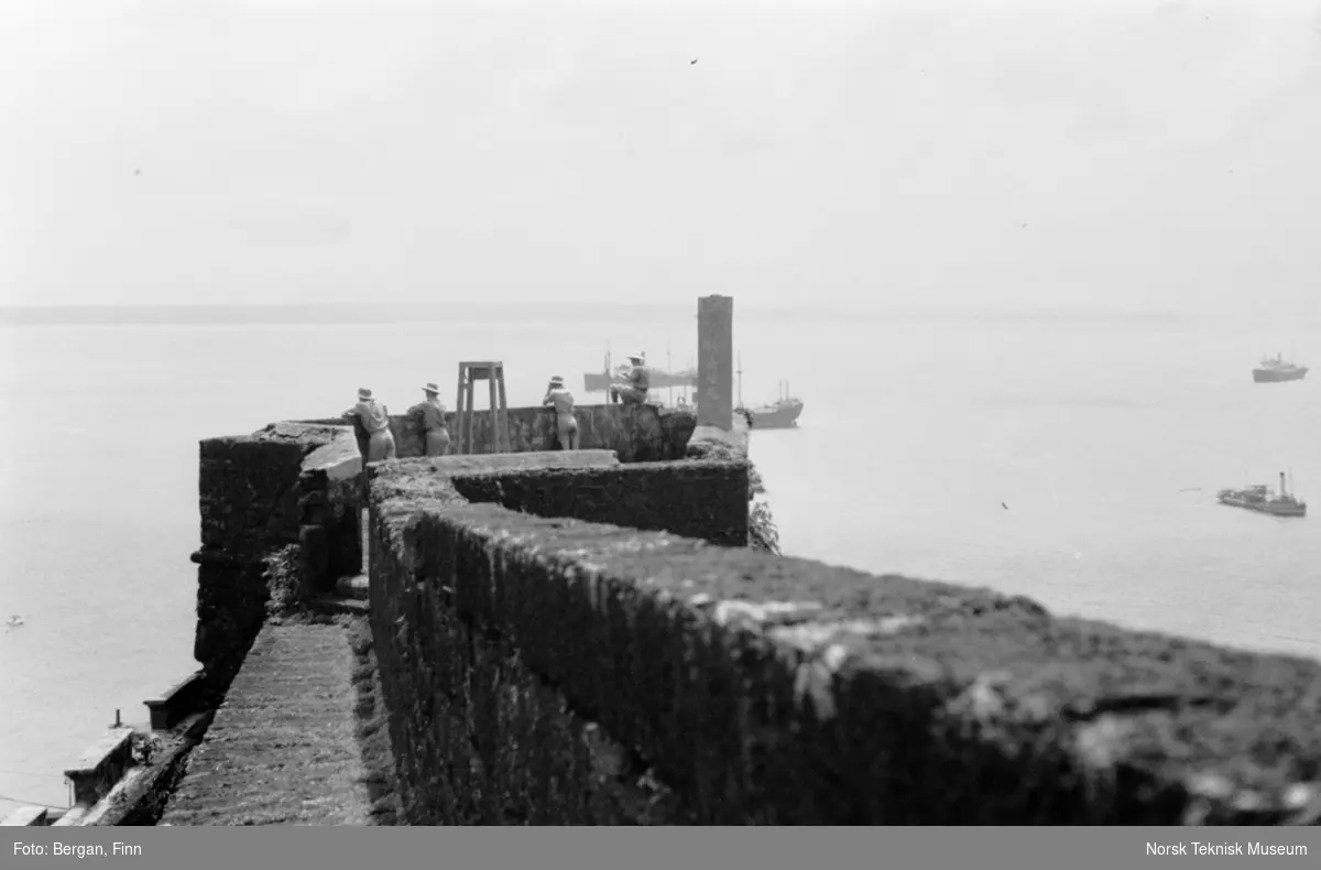 Festningsmur ut mot sjøen, fire personer på muren