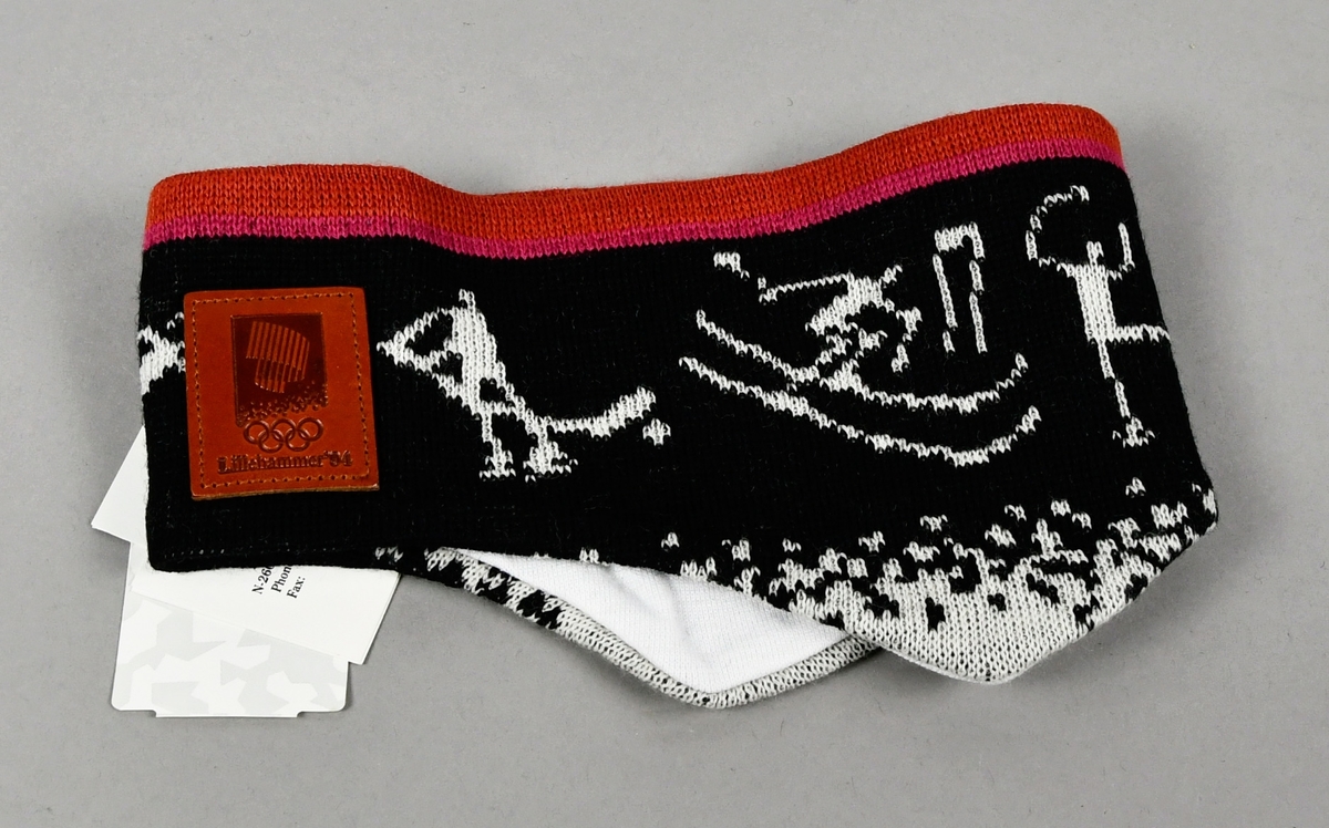 Svart pannebånd av ull med piktogrammer i hvitt. Pannebåndet er bredere på begge sider for å dekke over ørene. Midt foran er det et skinnmerke med logo for Lillehammer '94.