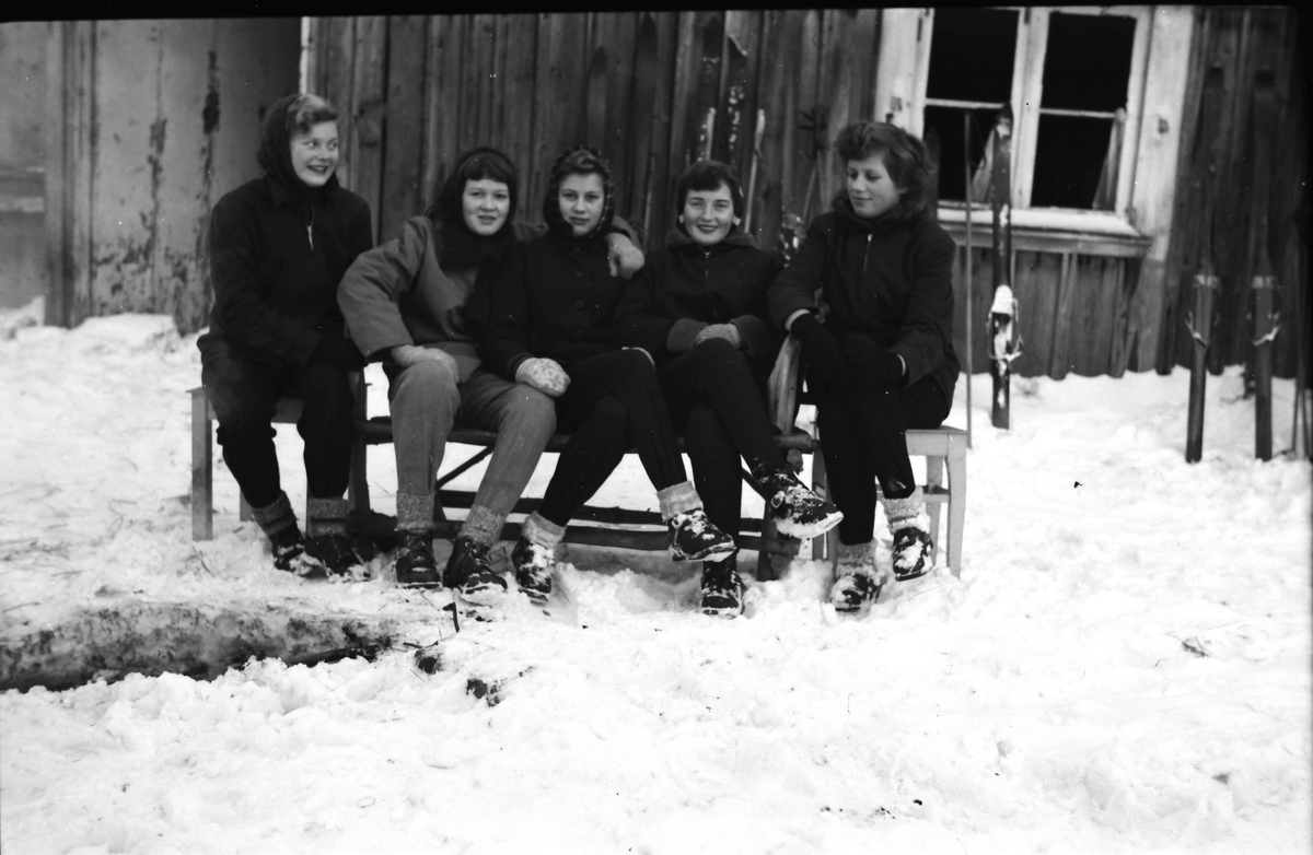 Fem skidåkerskor pausar på en bänk vid en stuga. Skidorna har de ställt mot husfasaden. Fr v Birgitta Andersson, okänd, Eivor Molin, Inga-Britt Albinsson och Gullan Molin.
(Se även bildnr EA1055, EA1059)