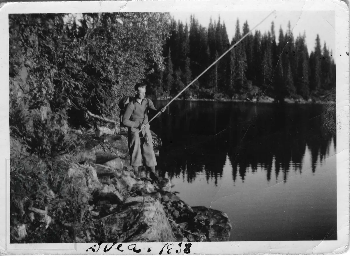 En mann står og fisker med bambusstang. Har et knippe med fisk.