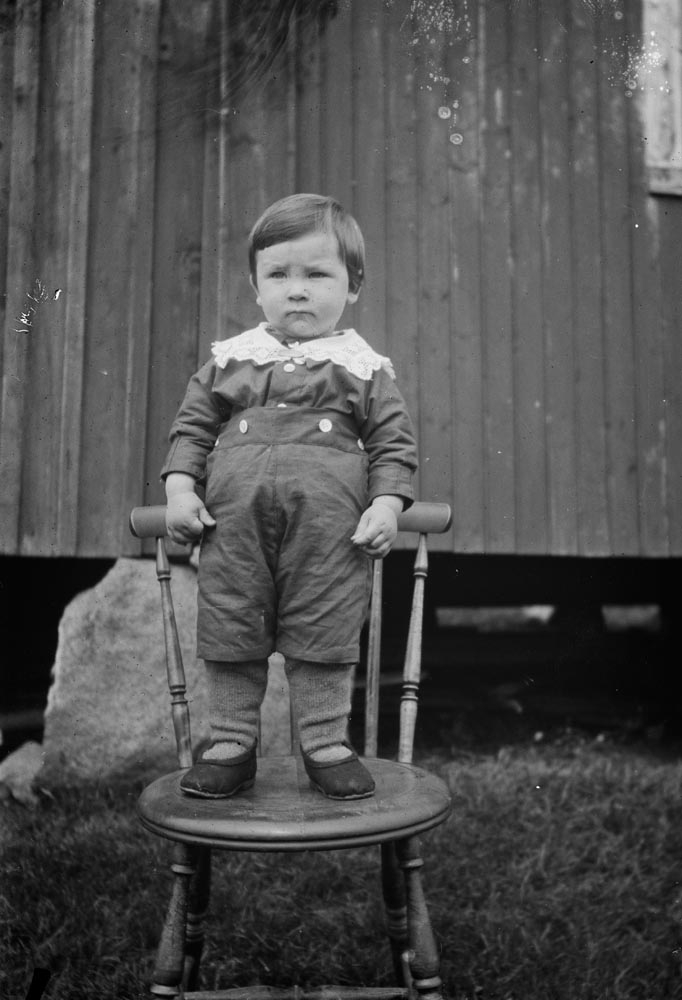 Leirfjord, Ulvangen, Myrvang. Portrett av liten gutt i barneklær stående på stol. Gutten er Johannes Jensen, sønn av Paula (f. Myrvang) datter til fotografen. Johannes er fotografert av sin morfar foran fjøset på Myrvang.