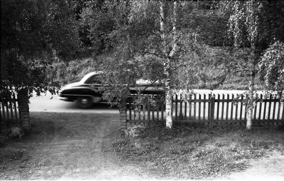 Bilde tatt fra gårdsplassen på Odberg på Kraby, Østre Toten, sommeren 1957. En bil passerer på daværende riksveg 33 (nå Totenvegen).
