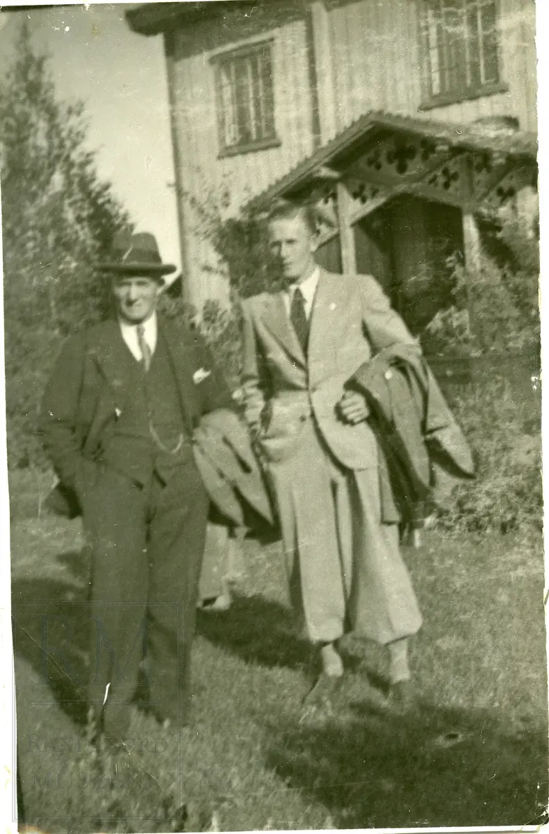 Petter Sinnerud og Hans Engnestangen stående utenfor et hus med utskjæringer i inngangspartiet.