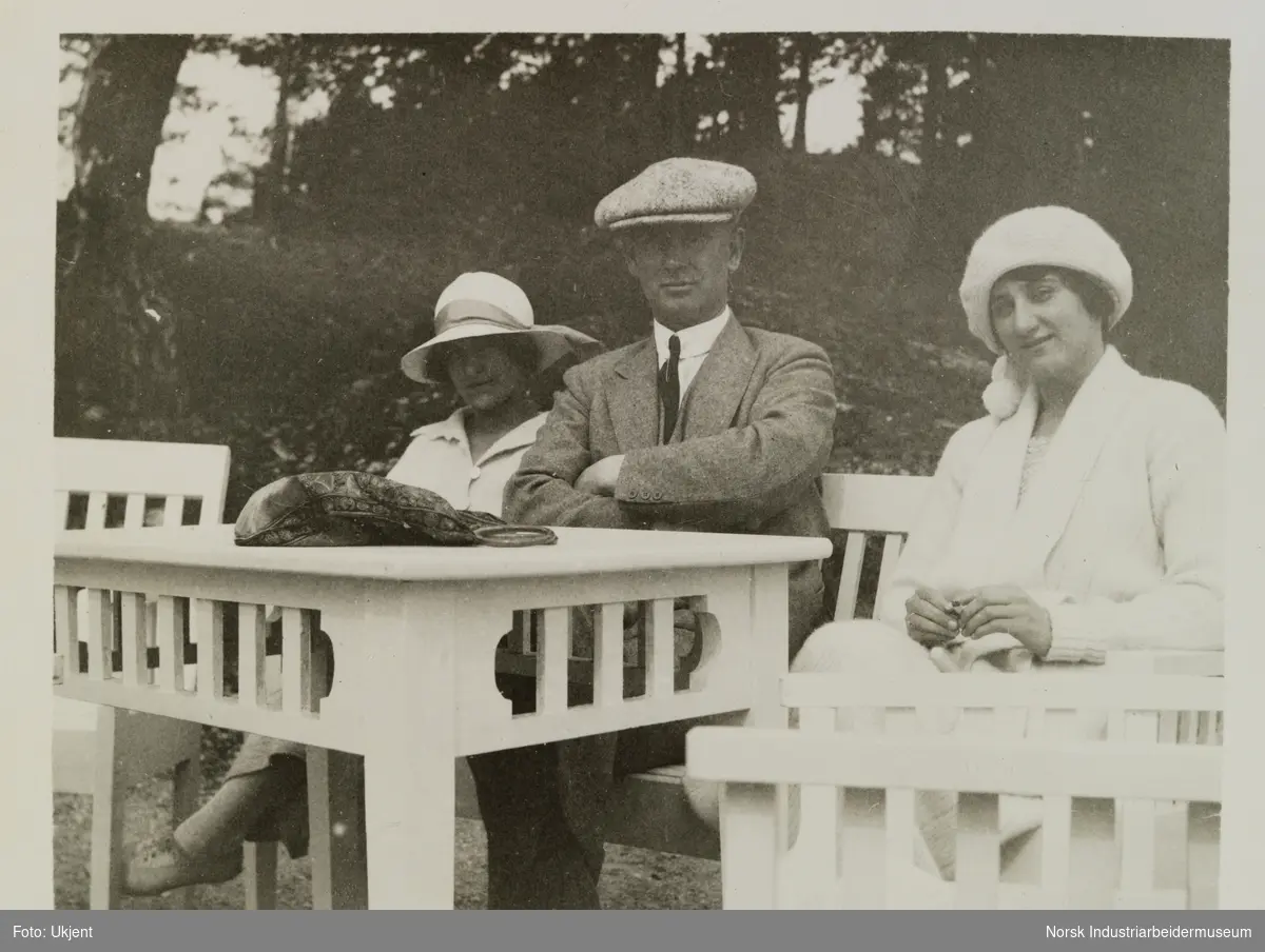 To kvinner og en mann sitter utendørs på hagemøbler