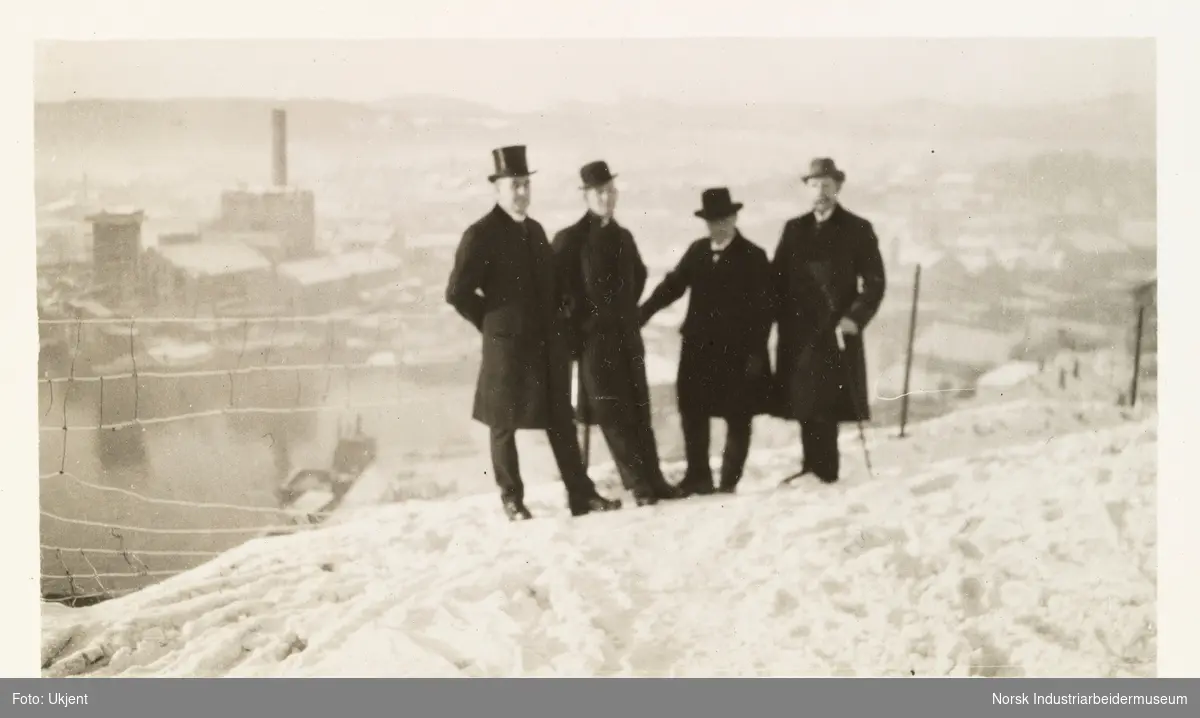 Fire menn med hatt på utkikkspunkt over by og industriområde