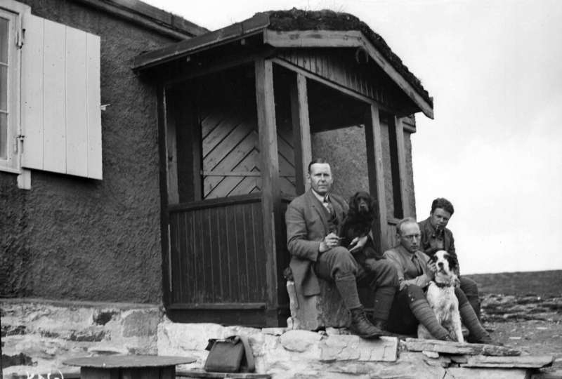 Ringebu. Flaksjøen. Jegere, tre menn med to hunder, foran Nils Anderssons hytte.