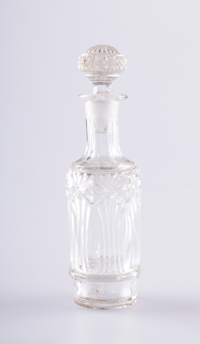 Flasken er regelmessig rund med slank hals og har en glasspropp. Flasken er dekorert med vertkale linjer, og blomster innrammet av ruter øverst. Glassproppen har en lignende blomsterkrans.