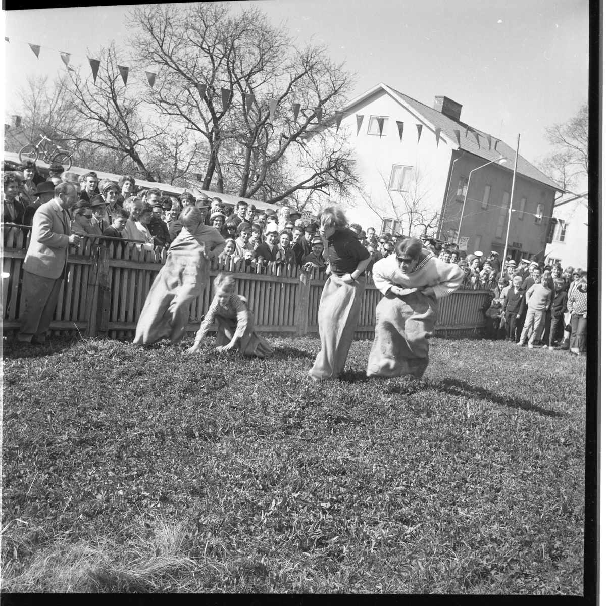 Barn hoppar säck på gräsmattan vid Sjögatan nedanför Brahegatan 37. Utmed ett staket står mycket folk och tittar på.