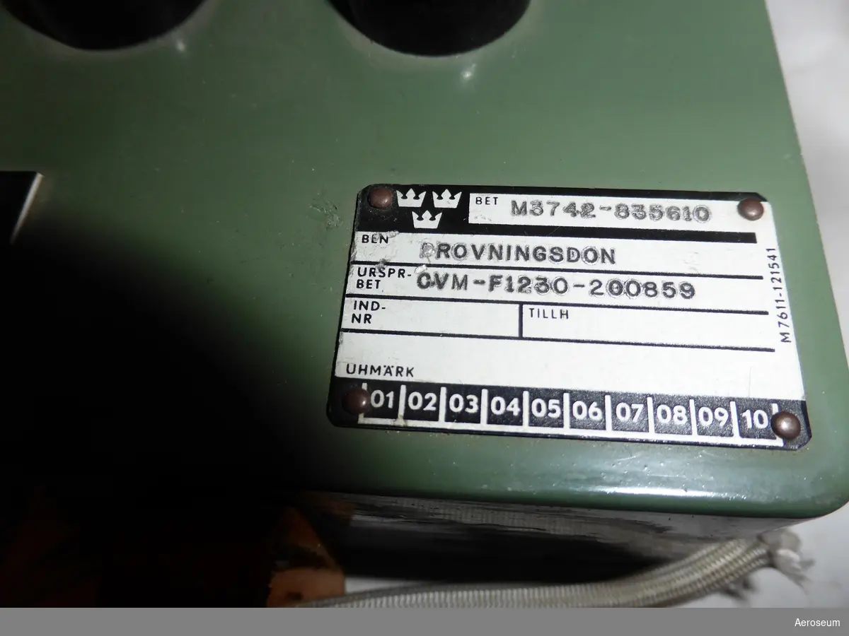 Ett provningsdon i grågrönmålad metall. Till för tidrelä vinsch på HKP4. På ena sidan står det inristat: "12 HKP DIV TELE". På botten av föremålet finns ett kretsschema ritat på en papperslapp fastklistrat. en grå sladd med ett vitt tygskydd sitter fast i föremålet och i slutet av sladden finns en grå kontakt med skruvbart skyddslock. 

Kopplat till föremålets M-nummer (M3742-835610) finns ritningsnummret "F1230-200859" kopplat, som även står med på en metallplatta som är fastskruvat på provningsdonet. Utöver det står ett annat F-nummer på papperslappen med kretsschemat: "F1230-403726".