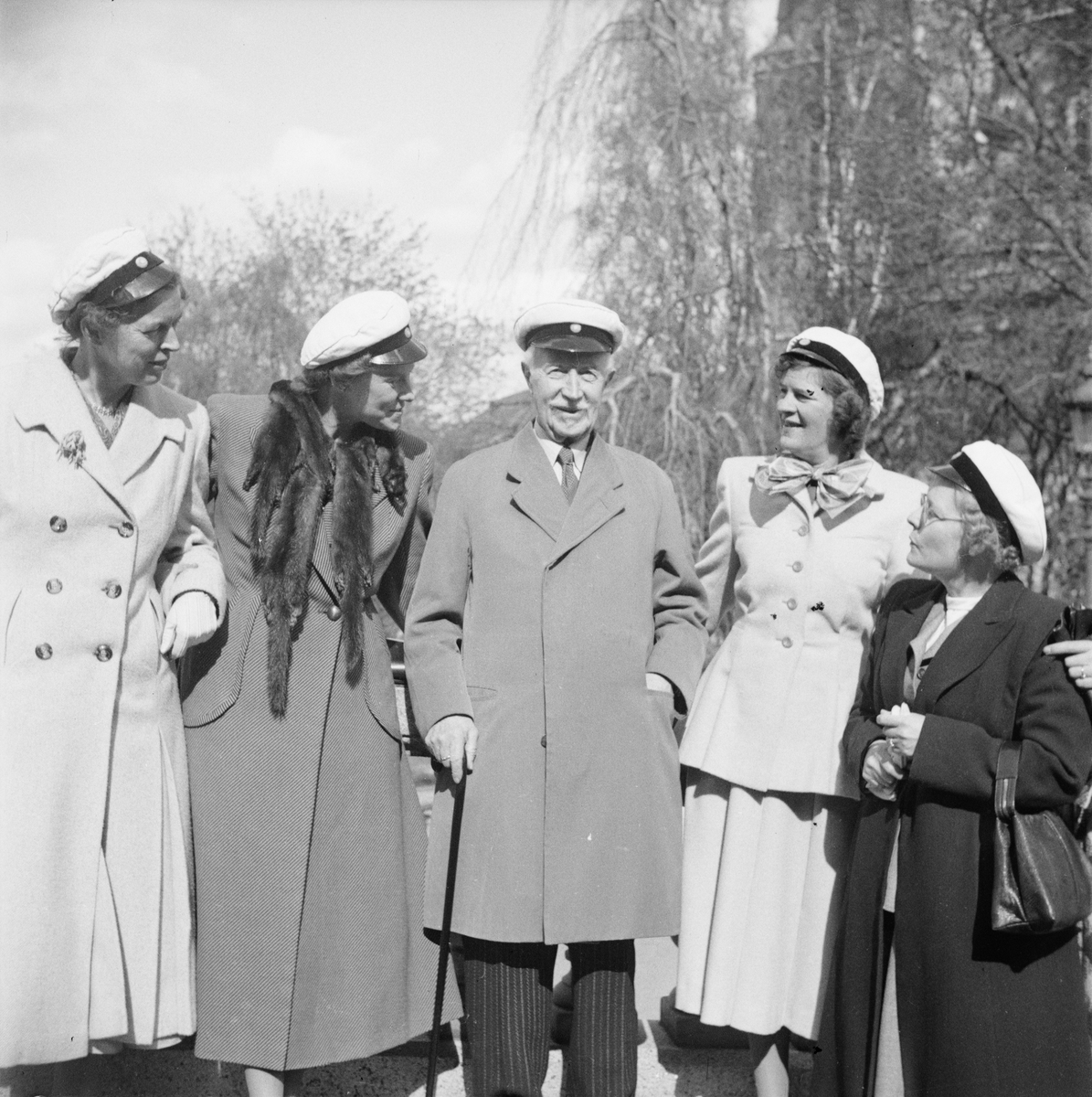 Fem personer med studentmössor vid Universitetsparken, Östgöta nations minneslandskap, Uppsala 1949