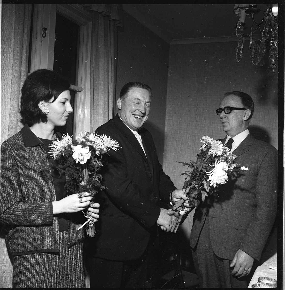 Lena von Essen med blommor i handen. Intill står en skrattande Ture Jägenstedt som troligen tagit emot en blomsterbukett och tackar Bertil Weinmer.