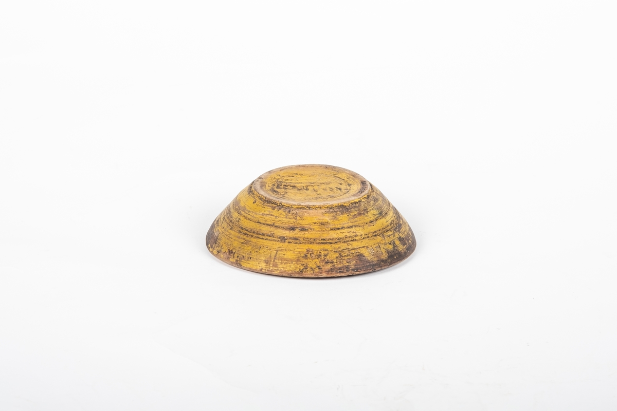 En liten rund treskål. Den er dreid og er malt gul på utsiden.