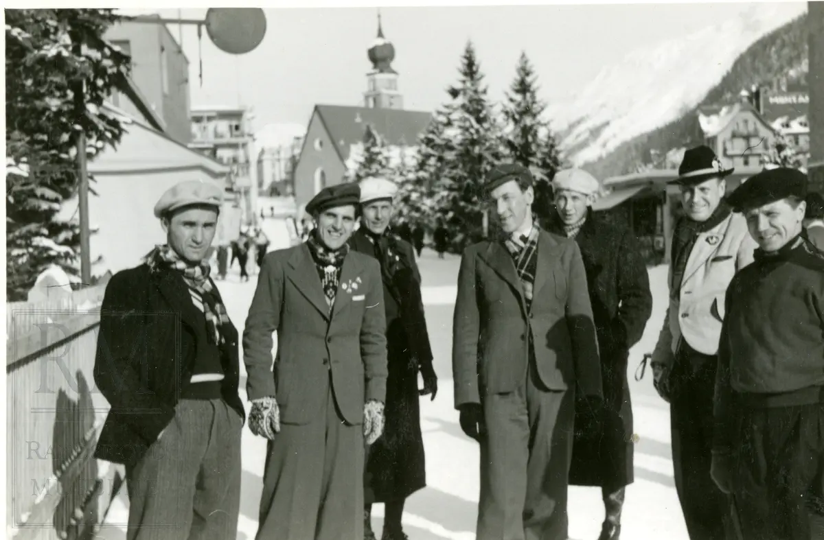 En gruppe menn, deriblant Hadelandstrioen, stående i ei gate med en kirke med løkkuppel i bakgrunnen.