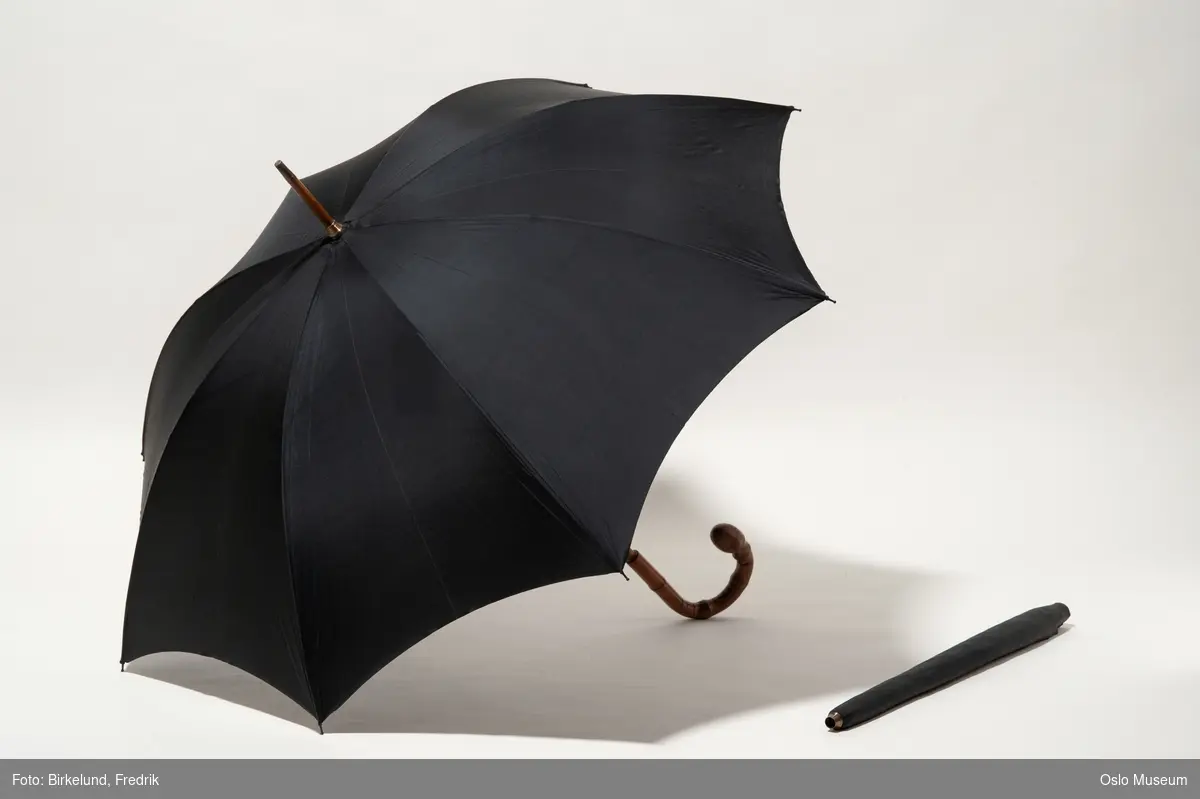 A.Paraplyen: Skaft og stokk av beige bambus, dopsko av messing. Stellet=spilene av sortmalt stål,skjermen av sort silke. 
B.Trekket: Lang,smal poseform, nederst messingbeslag, øverst lukning m. trykknapp. Stoff som skjermen.