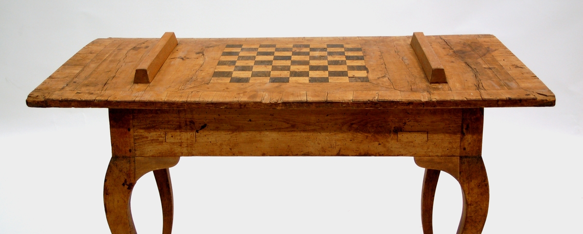 Brädspelsbord, från 1700-talets förra del. Rokokomässigt svängda ben. Locket som är en lös skiva har intarsia i form av en schackspegel. Själva bordet, som har en tvärslå på mitten, har trekantiga spelfält i intarsia. Intarsian svart och gulvit.
Bordets längd 95cm bredd 55cm höjd 75cm. Skivans längd 125cm bredd 68cm.