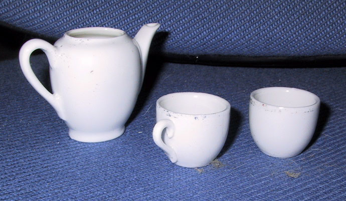 Kaffekanne (a), kopp (to) og skål i hvitt stentøy med påmalt blomst. Koppene har noen rester av rand, litt rødt.