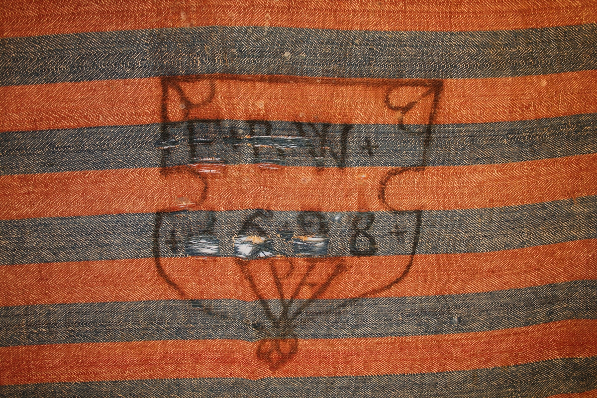 Vevd altarduk, to fargar (raud og blå). Trykk/monogram på midten, delvis uleseleg/slitt.