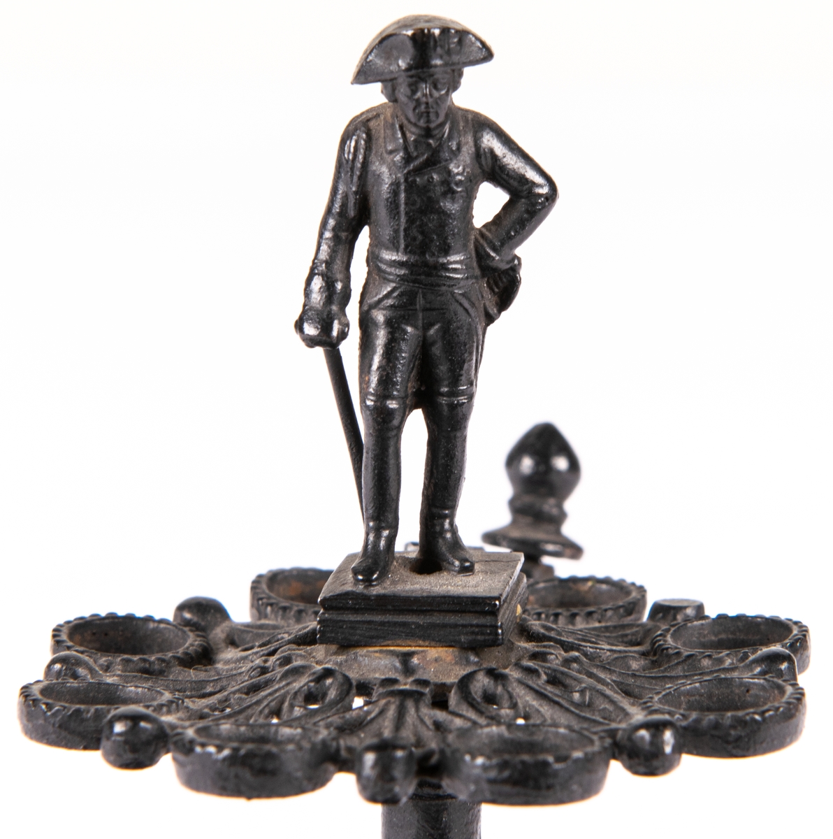 Cigarrställ med cigarrsnoppare på sidan. Av svartlackat gjutjärn. Könt med modell av Fredrik den store av Preussen.