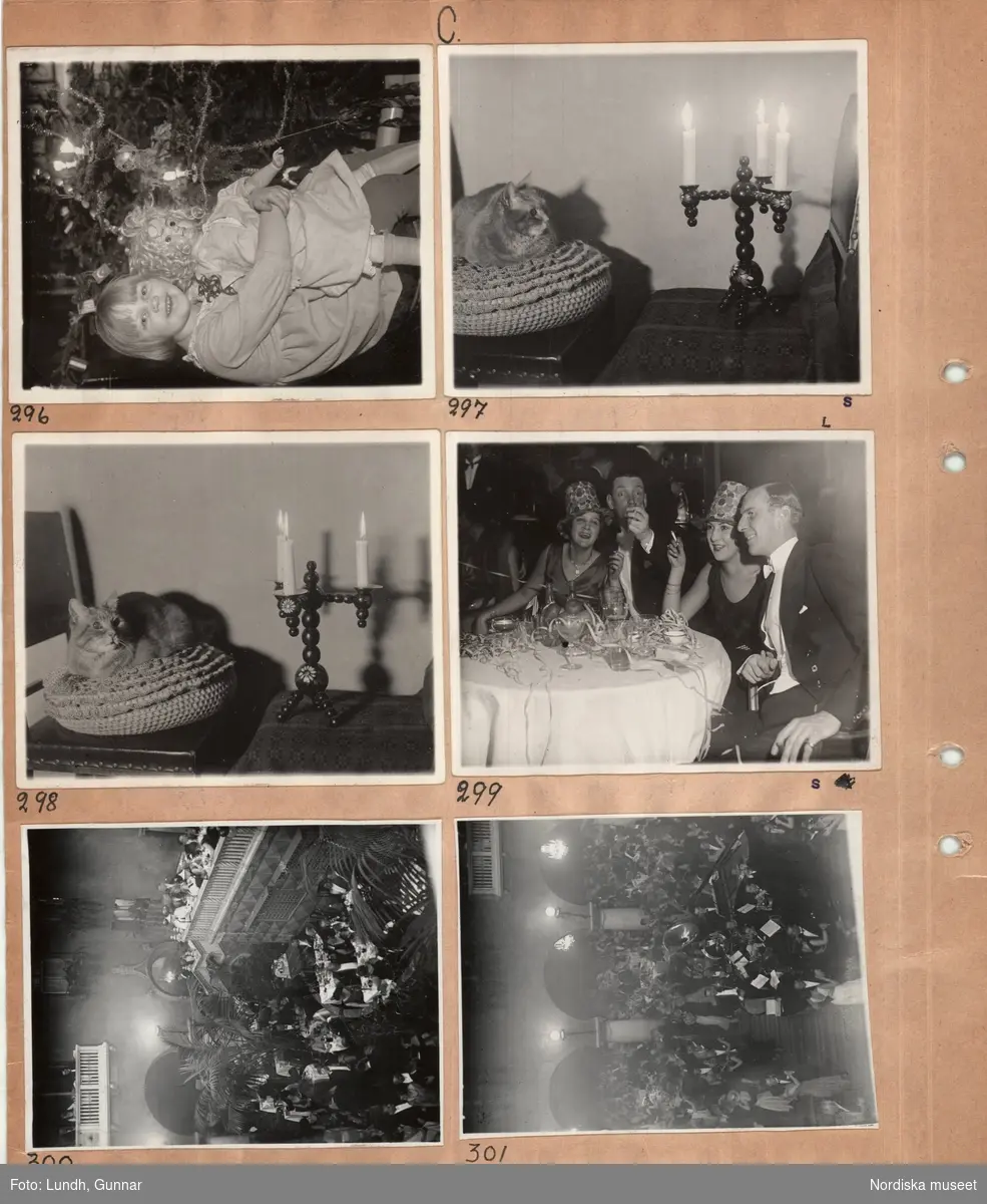 Motiv: (ingen anteckning) ;
Interiör med en flicka som sitter vid en julgran och håller en docka, en katt sitter på en kudde vid en ljusstake, interiör troligen från Grands Vinterträdgård med festklädda människor som sitter vi bord och äter och en orkester som spelar - möjligen vid nyårsfirande.
