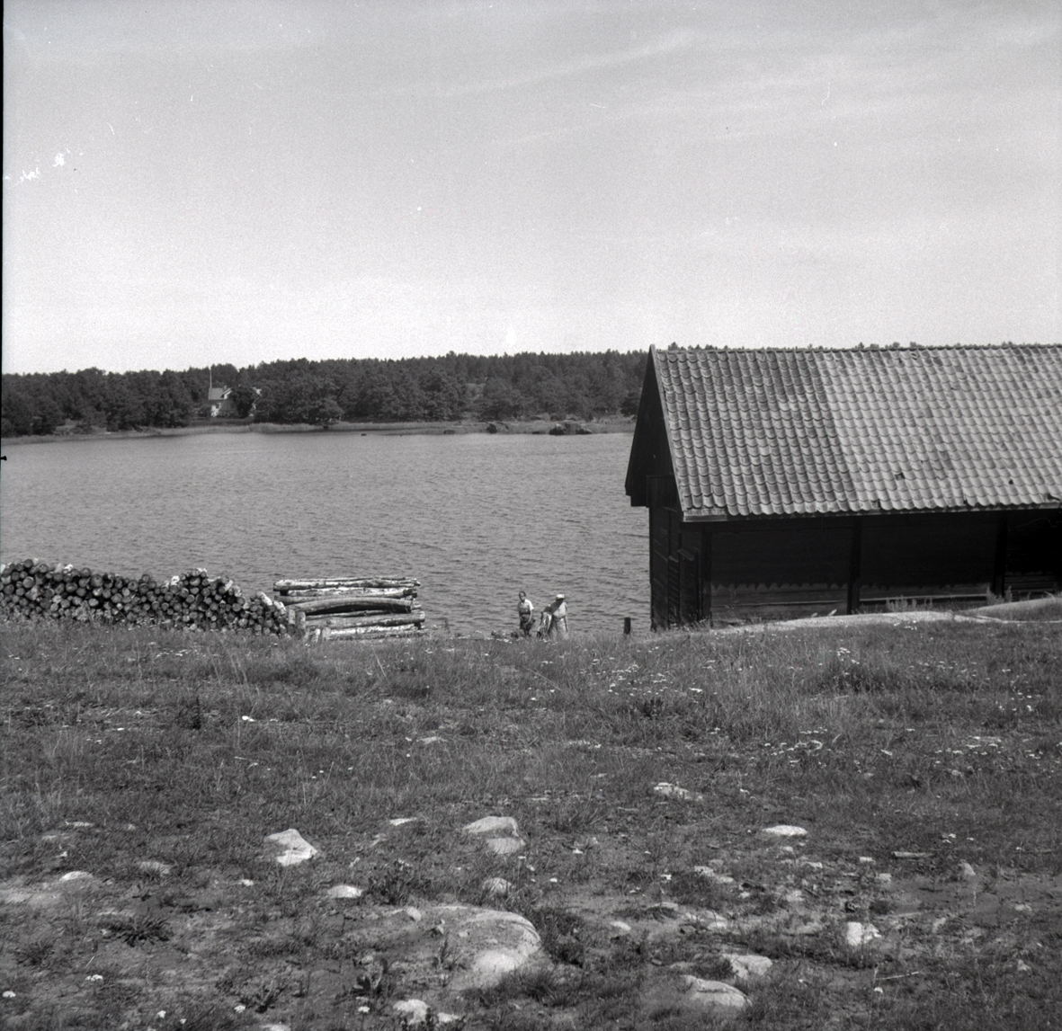 Misterhults socken, Kärrviks hamn, två kvinnor vid sjökanten, samt timmer och sjöbod.