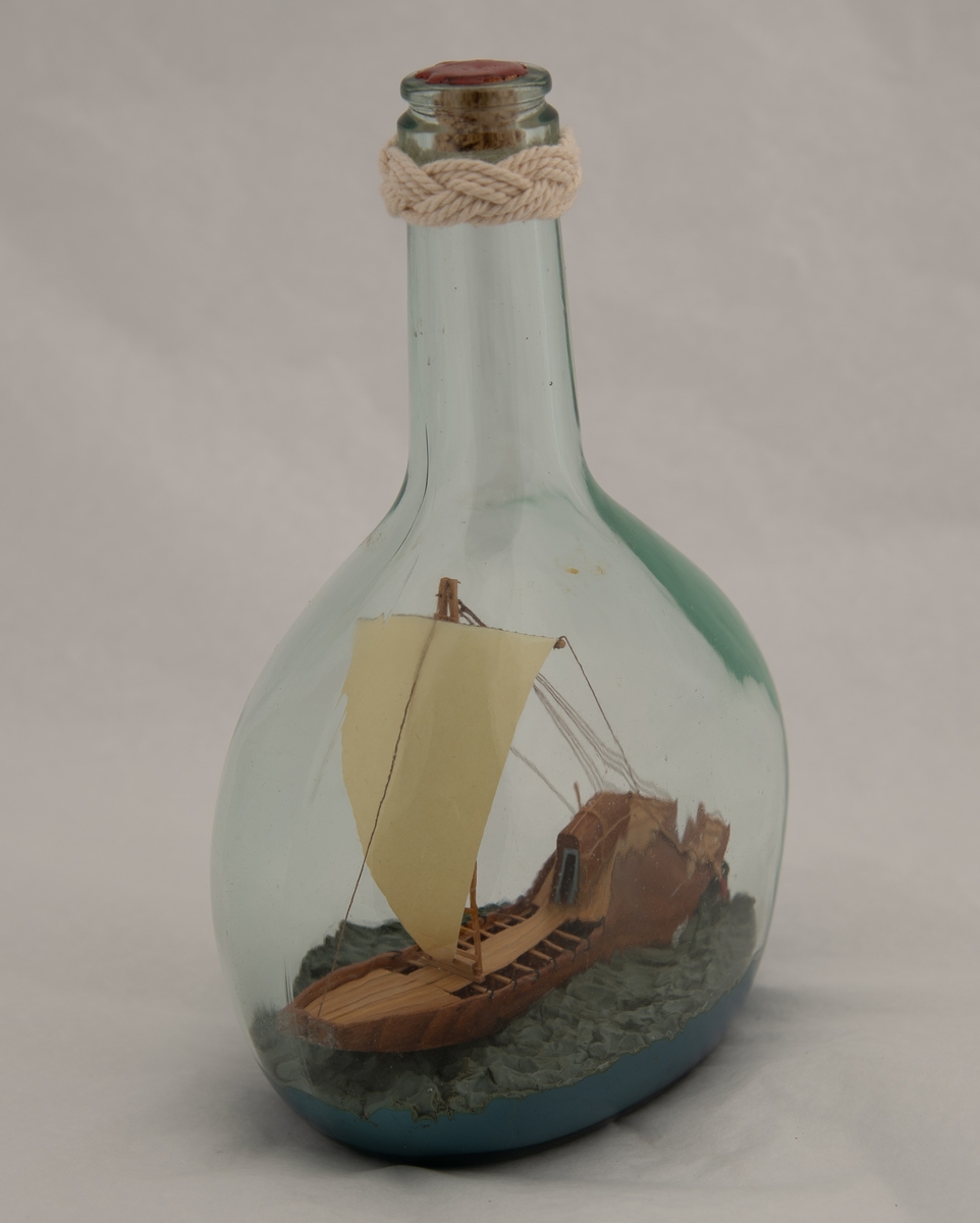 Flaskeskute: Egyptisk fartøy 1565-1080 f. Kr.  Flaske av klart glass (likørflaske) , innst. i bunnen 380 og g F. Oval bunn , flat på to sider , skrå skuldre , hals med en knop i seilgarn , munningen tettet med rød lakk. Bredbunnet skip , flatbunnet med trekantet seil , to styreårer bak og kahytt akter.