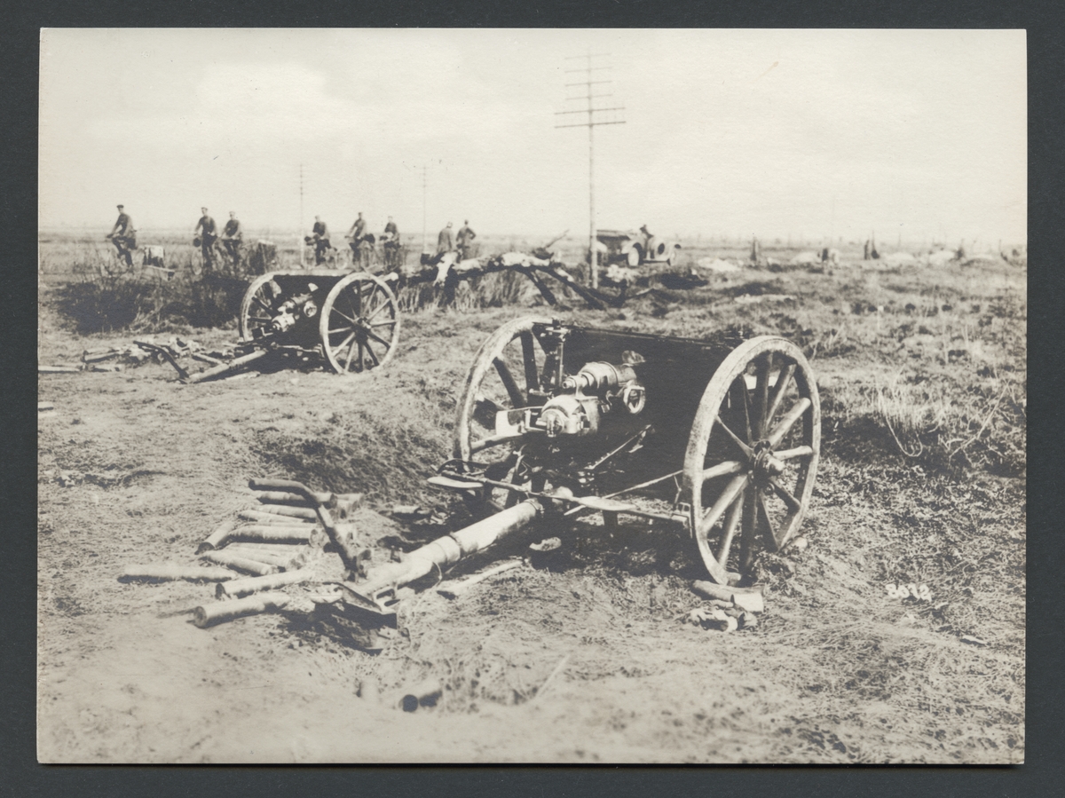 Bilden visar två övergivna artilleripjäser på slagfältet. I bakgrunden passerar en grupp soldater på cyklar.

Originaltext: "Stormad engelsk batteriställning på vägen till Avre."