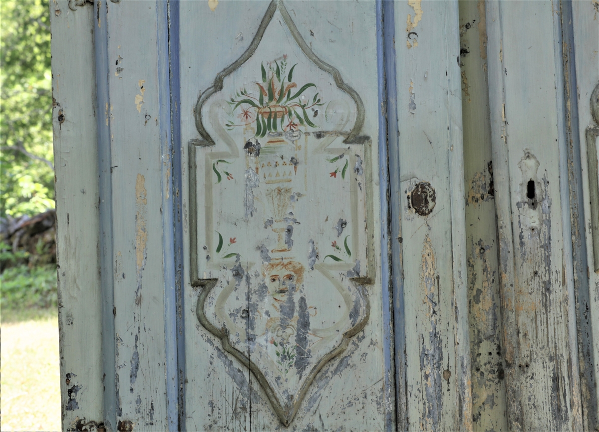 Skap med to låsbare dører. Malt i lyseblå, grålig farge og begge dørbladene dekorert.  men malinga er defekt.