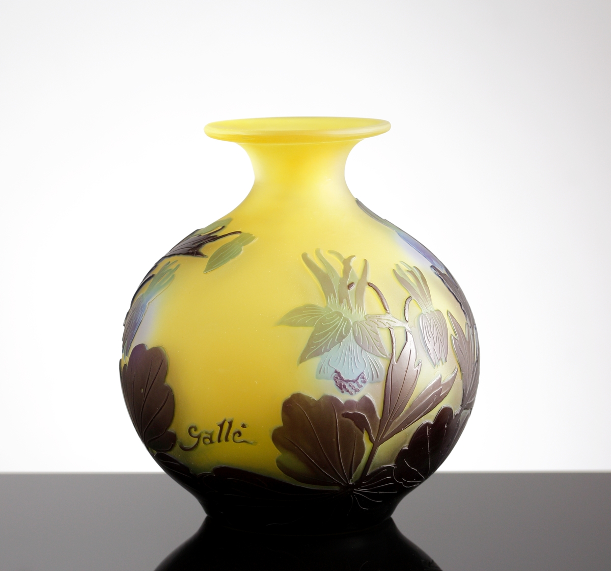 Halvopak, gul vas med etsat överfång i blå- och grönblå nyanser. Växtmotiv med blommor och blad.