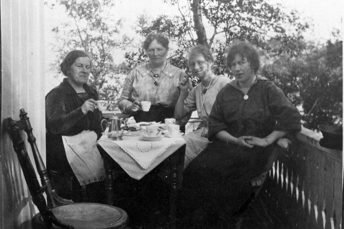 Gruppeportrett av fire kvinner som drikker kaffe på veranda.