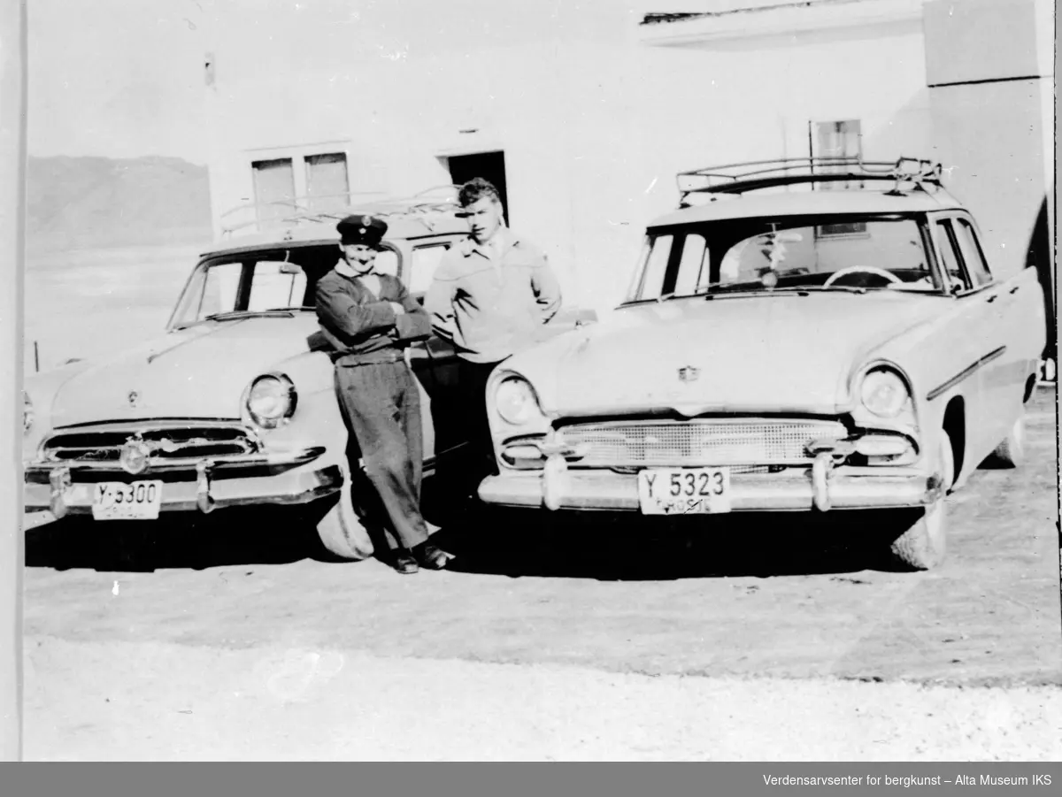 To sjåfører med to biler utfor den gamle drosjeholdeplassen med en Chevrolet og en Dodge. De to mennene lener seg intil den ene bilen.