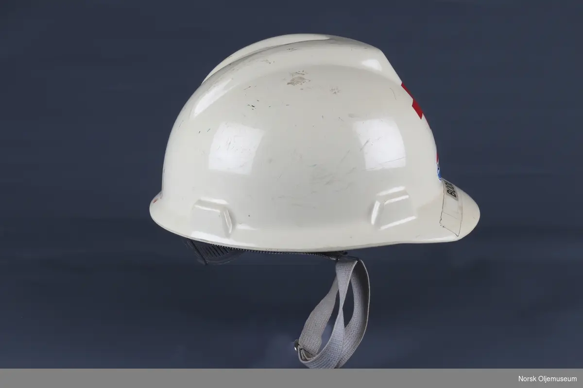 Vernehjelm med innvendig hjelmhette. Hjelmen har Amoco sin logo og klistremerke med navn foran. 

Hjelmen var en del av utstyret tilknyttet sykestuen på boligplattformen QP på Friggfeltet.