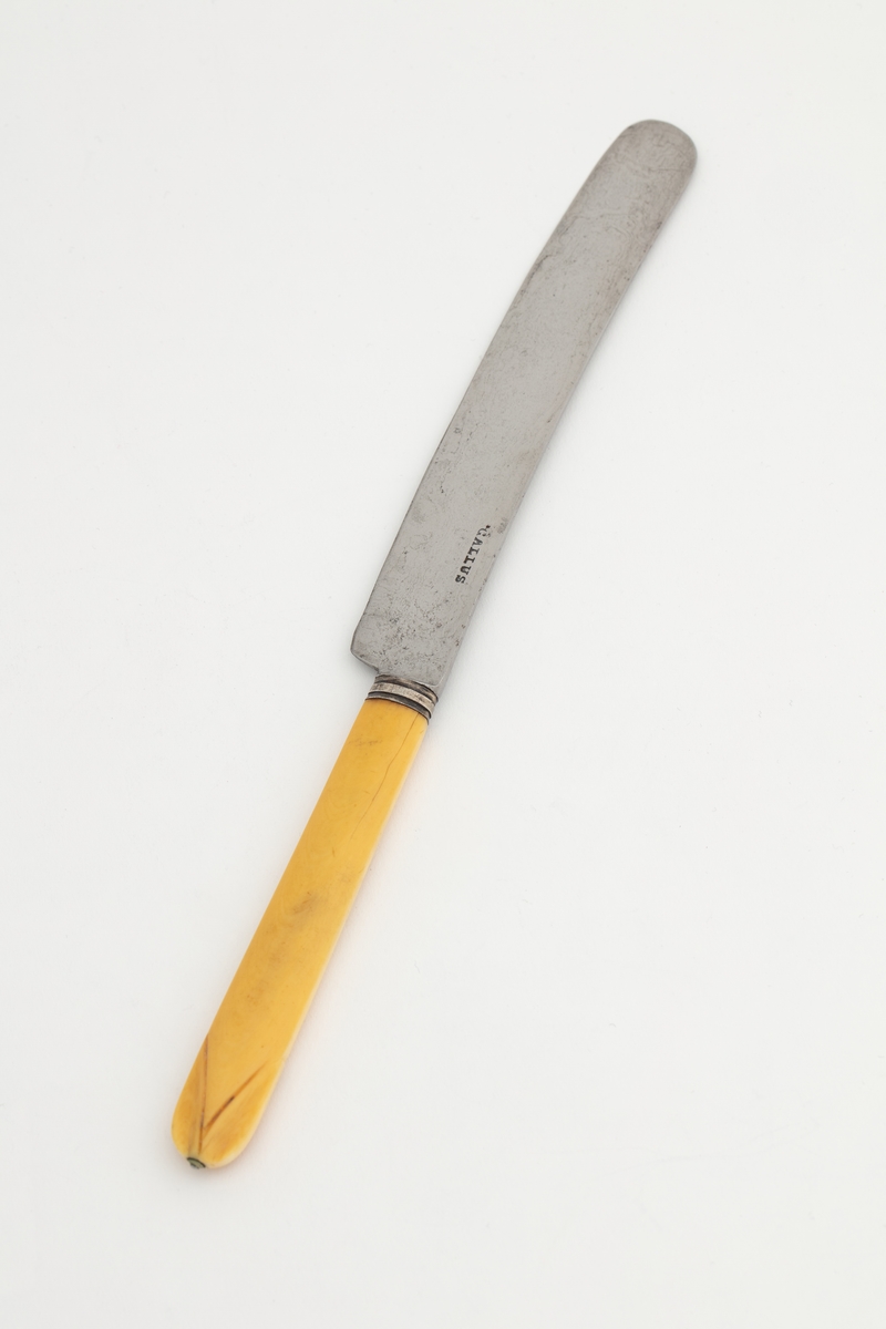 Avrundet knivblad av stål stemplet «Gallus». Holk med to konsentriske, innrissede streker. Skaft av bein, svakt avspisset og nedsenket øverst med to diagonale streker og liten, innfelt «doppsko» (nagle) av stål på tuppen.