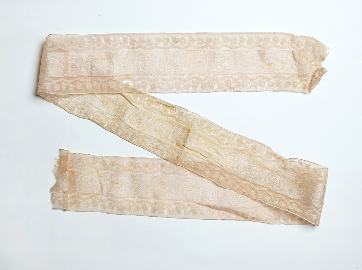 Bredt silkebånd med damaskmønster i midten og mønster op gjennomsiktig bunn i kanene.