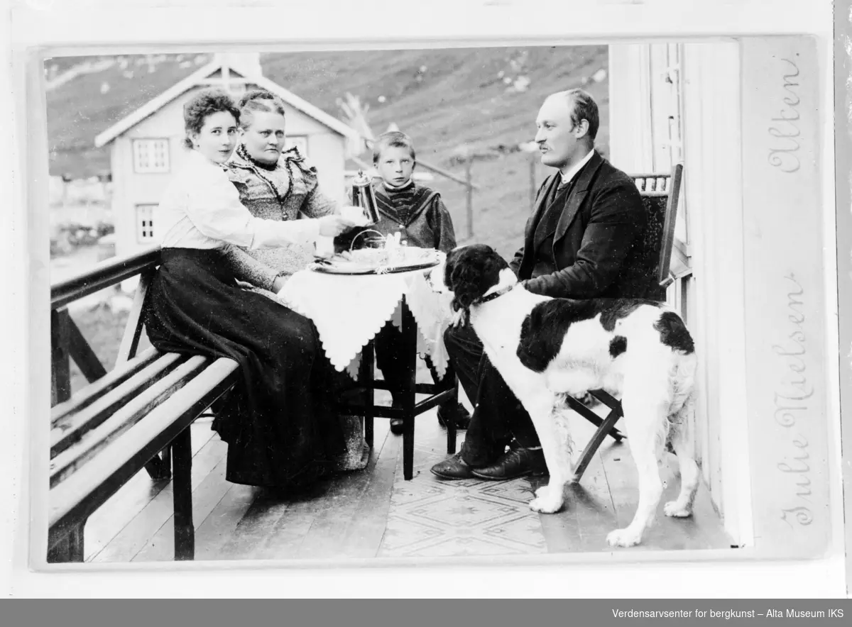 Kaffeselskap i Komagfjord, 4 personer med hund sitter rundt et bord på en veranda og drikker kaffe.