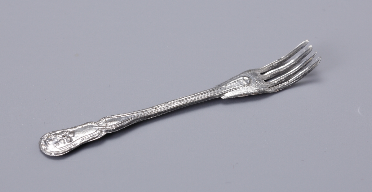 Dockbestick, kniv och gaffel i mjuk metall med lite ornament på skaften.

Inskrivet i huvudbok 1943.