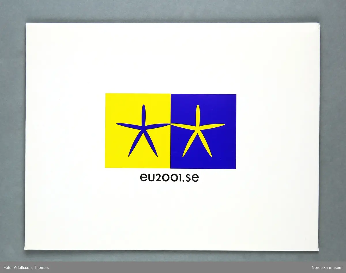 a) Scarf för kvinna. Avlång, rektangulär. Orange, tunt siden med tryckt mönster i mörkare orange med den officiella logotypen för Sveriges ordförandeskap i EU 2001.  I b) rektangulärt, kuvertformat fodral av vit kartong med tryckt logotyp i blått och gult, samt text ”eu2001.se”. Vidsydd lapp med texten ”PURE SILK/MADE IN/THE E.U.2 samt tvättanvisning. I rektangulärt, kuvertformat fodral av vit kartong med tryckt logotyp i blått och gult, samt text ”eu2001.se”.
/Annika Tyrfelt 2013-06-27