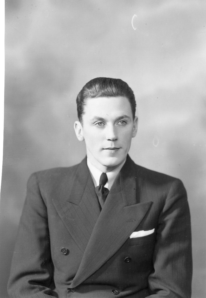 Porträtt av Stefan Ellbrant, en ung man i dubbelknäppt kostym, ljus skjorta, mörk slips och näsduk i bröstfickan.
