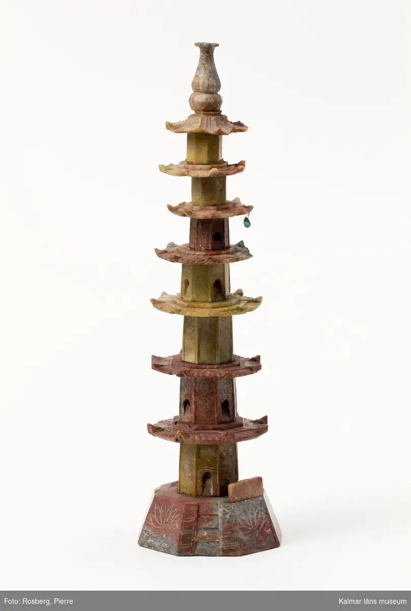 KLM 11674. Skulptur. I flerfärgad jade, röd, orange och grå. I form av ett torn med pagodtak. 7 våningar högt med en grön pärla hängandes i smal ståltråd på tredje taket uppifrån.